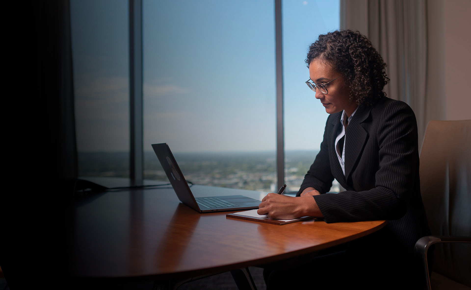 Businesswoman wearing suit writing on a legal pad in an office boardroom.